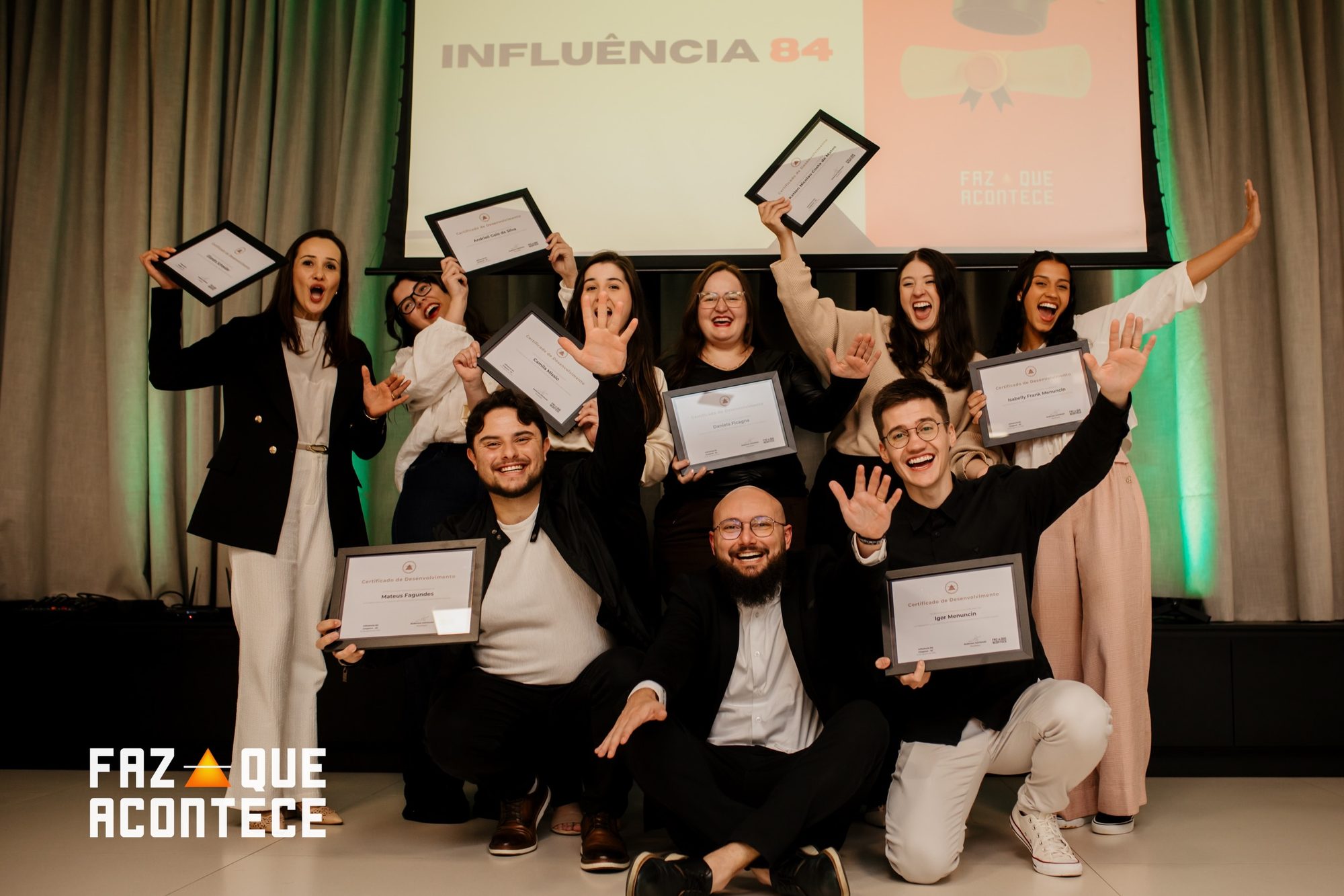 Turma erguendo os certificados no palco, no dia da formatura